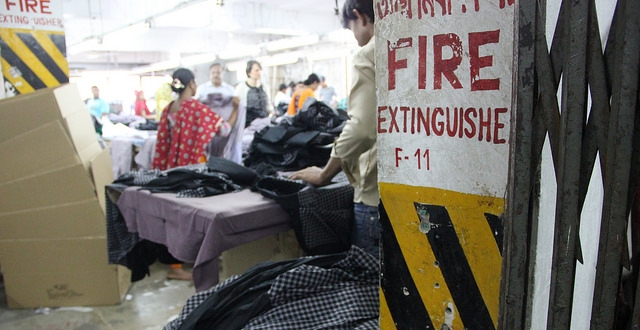  A fire extinguisher is conspicuously absent inside a factory where clothing and boxes, potential fuel sources, are stacked on the floor. Photo Credit Bishawjit Das.         